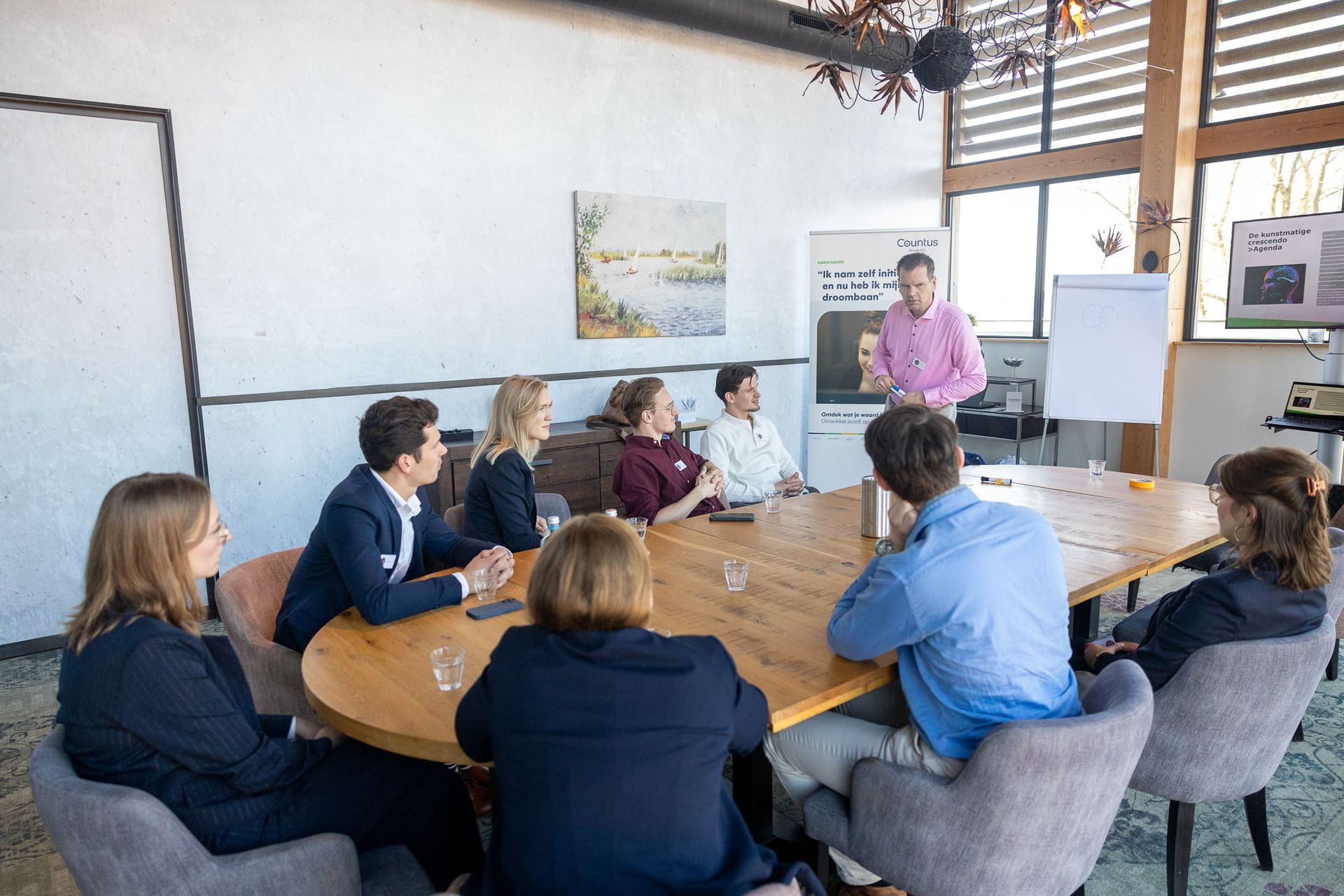 Een groep mensen in een vergaderruimte luistert naar een presentatie. Een man staat bij een whiteboard.