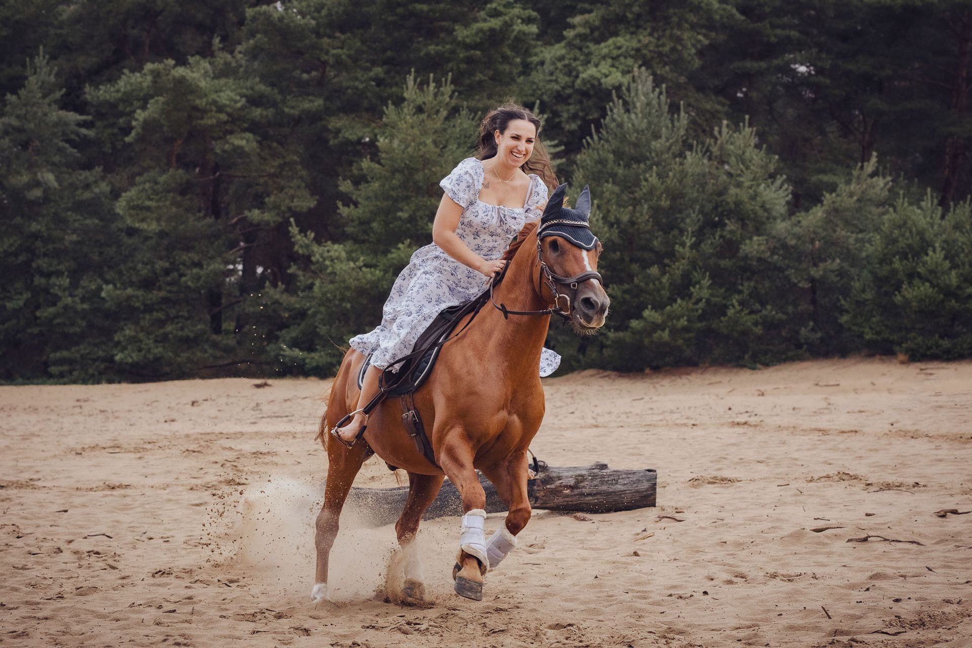 Vrouw rijdend op een kastanjebruin paard in een zanderig gebied. Het paard draagt ​​een hoofdstel; de vrouw draagt ​​een jurk met bloemen. Bomen op de achtergrond.