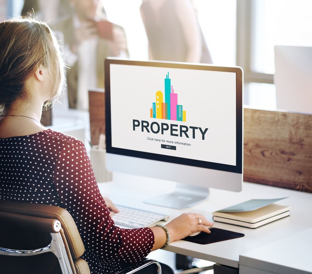 Woman at a computer, viewing a property website with a cityscape graphic, in an office.