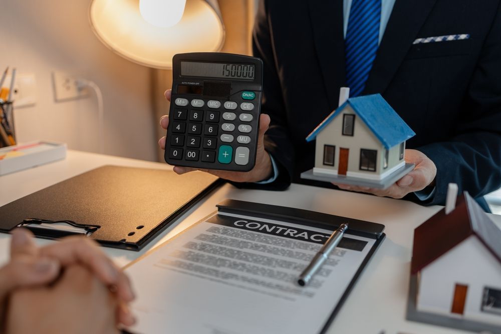 Person showing calculator and house model over a contract. Desk setting.