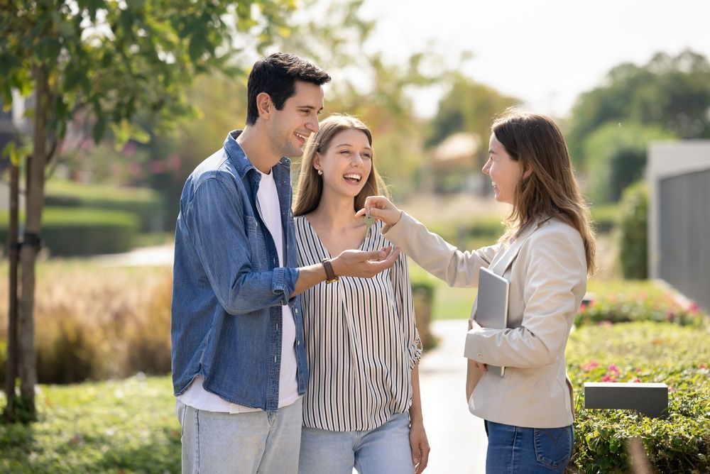 A realtor gives keys to a smiling couple outside a modern building.