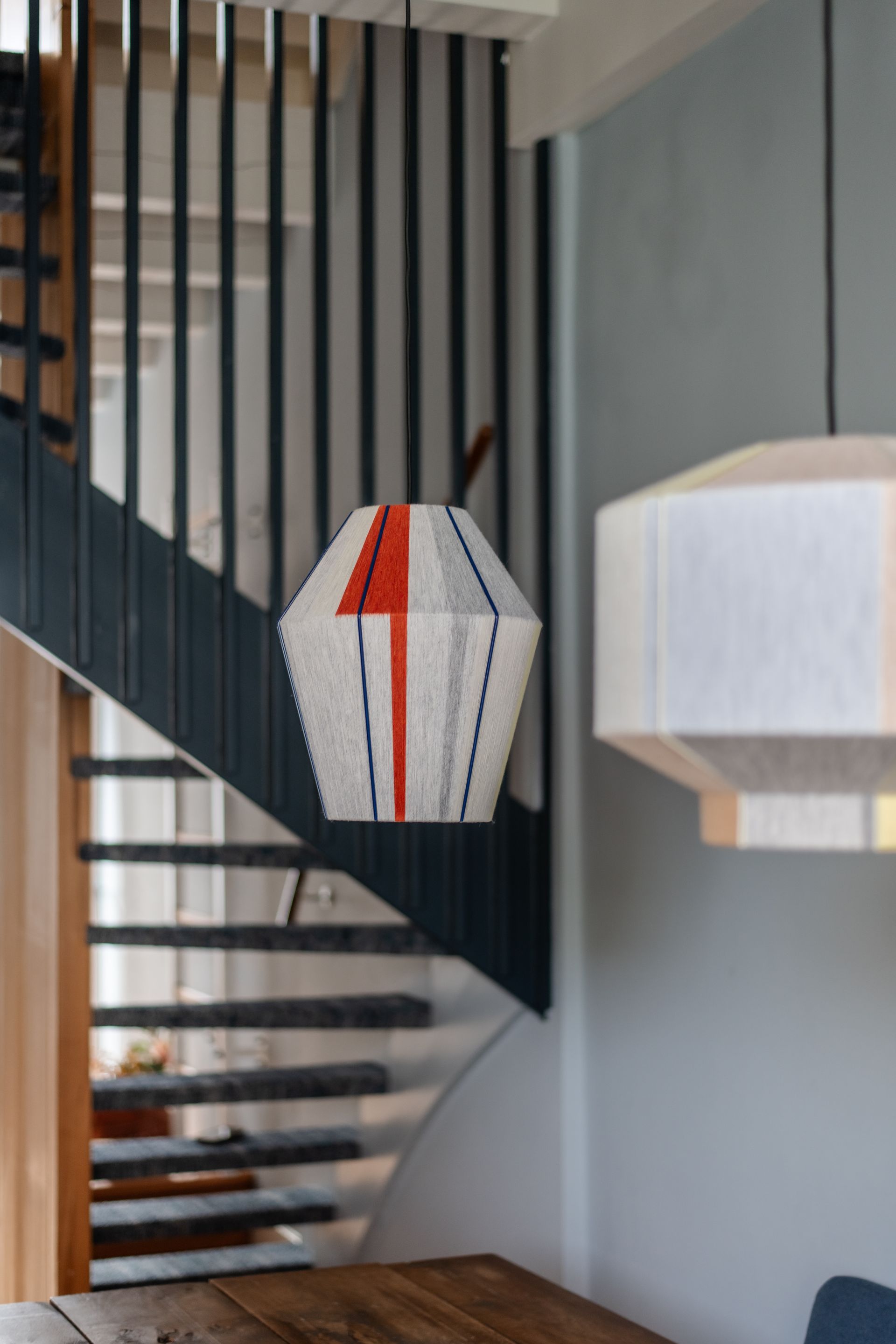 Trap met donkerblauwe leuning en hangende geometrische hanglampen, waarvan één met een rood pijlontwerp.