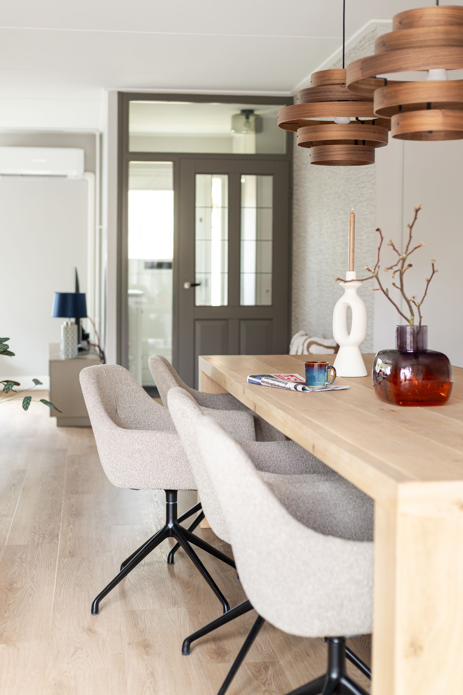 Eetkamer met houten tafel en stoelen, hanglampen en decoratieve objecten.