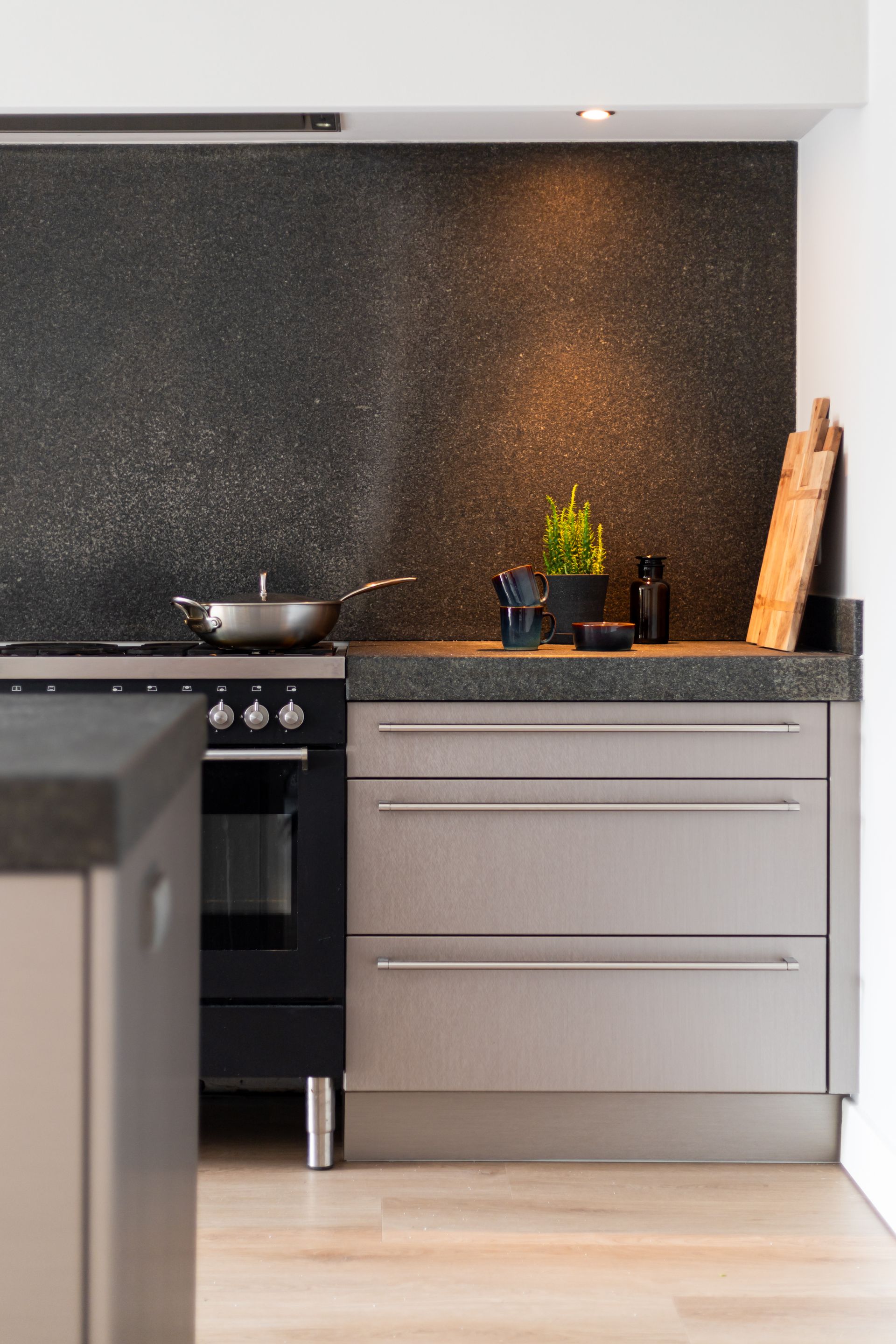 Moderne keuken met zwarte achterwand, roestvrijstalen apparatuur en grijze kasten.