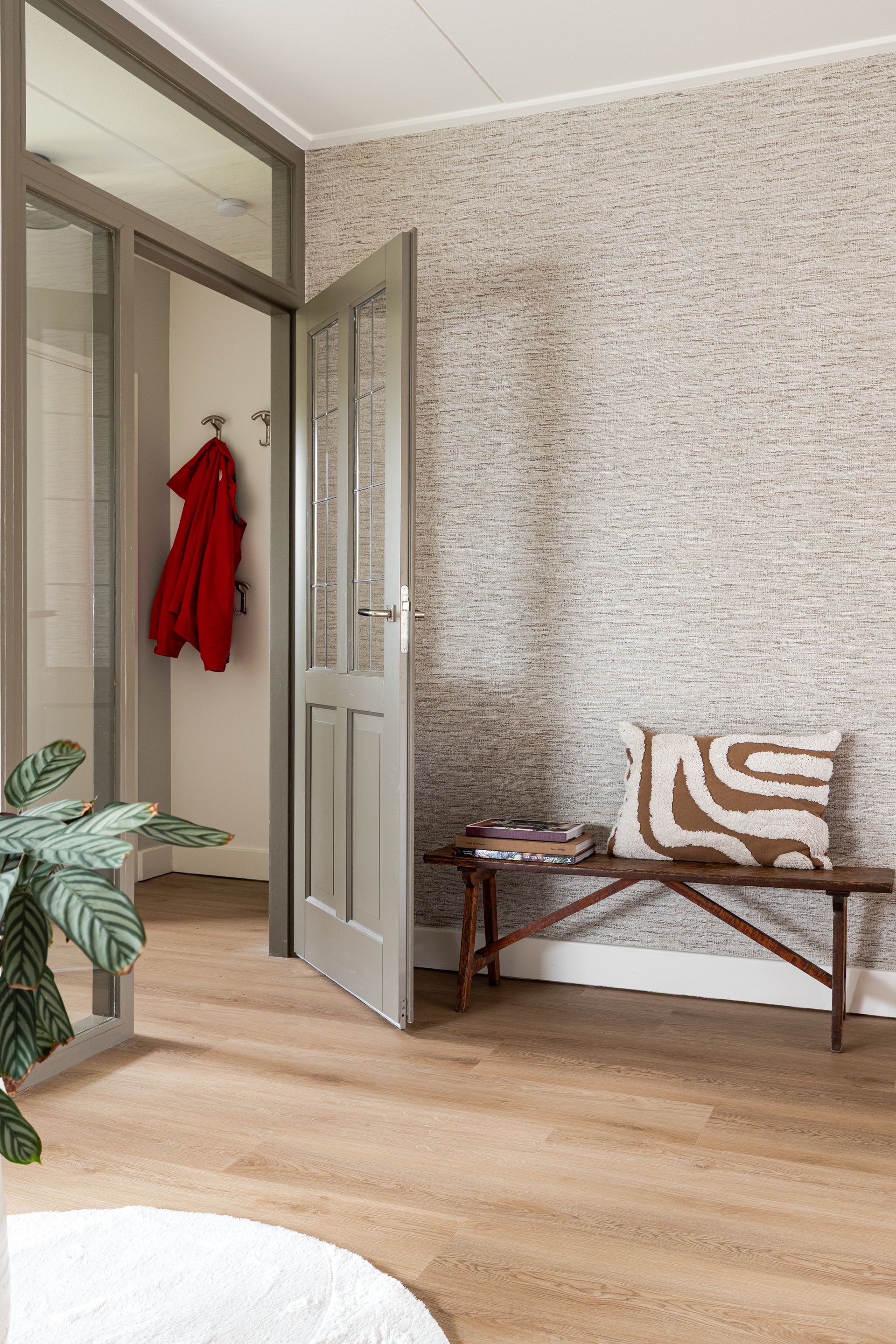 Hal met behang met patroon, houten bank, open deur naar garderobekast, rode kapstok.