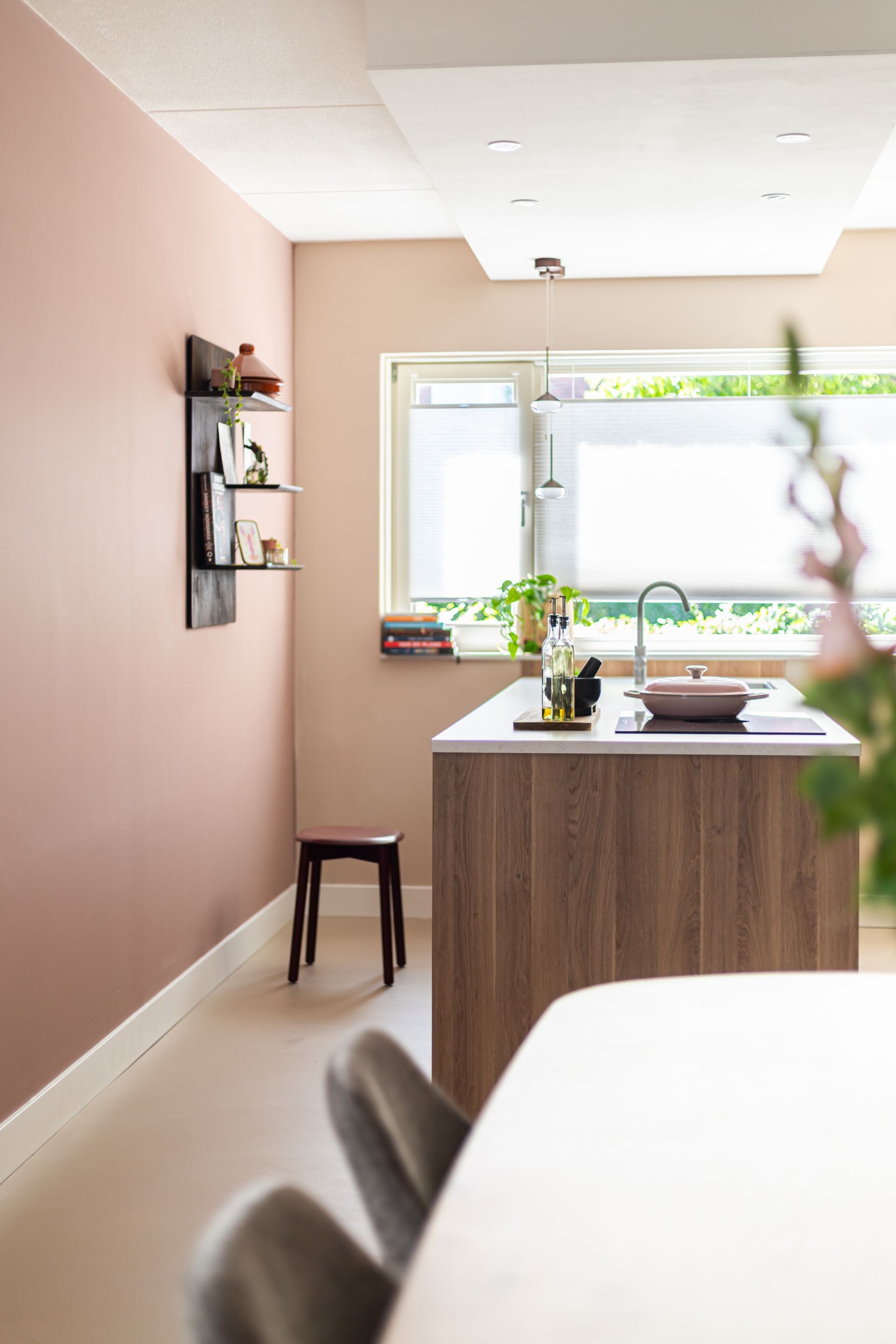 Keuken met roze muur, houten kookeiland, raam en klein krukje.