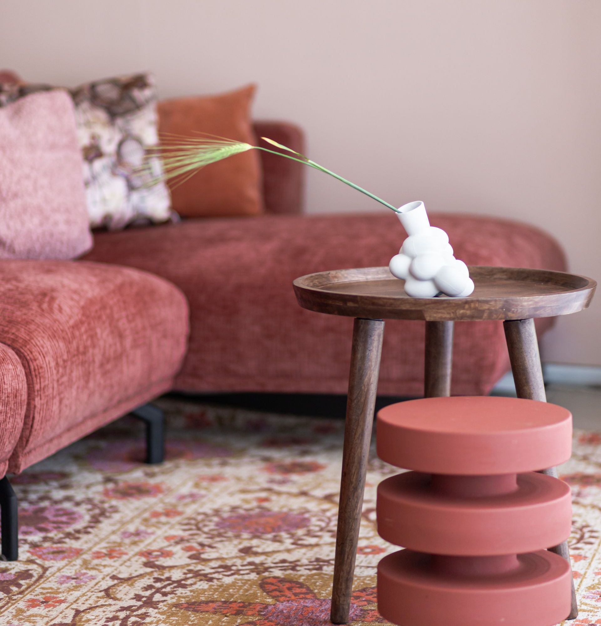 Woonkamer met koraalkleurige bank, houten tafel met vaas en tapijt met patroon.