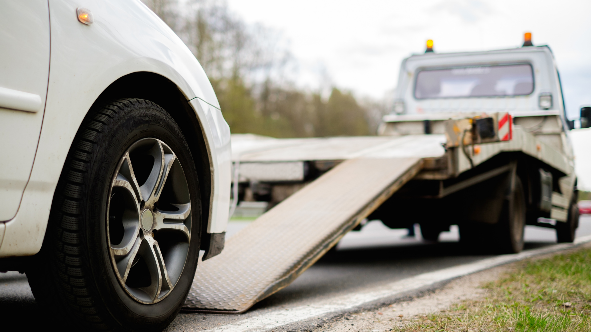 Silver car loaded on a red tow truck on a sunny road.