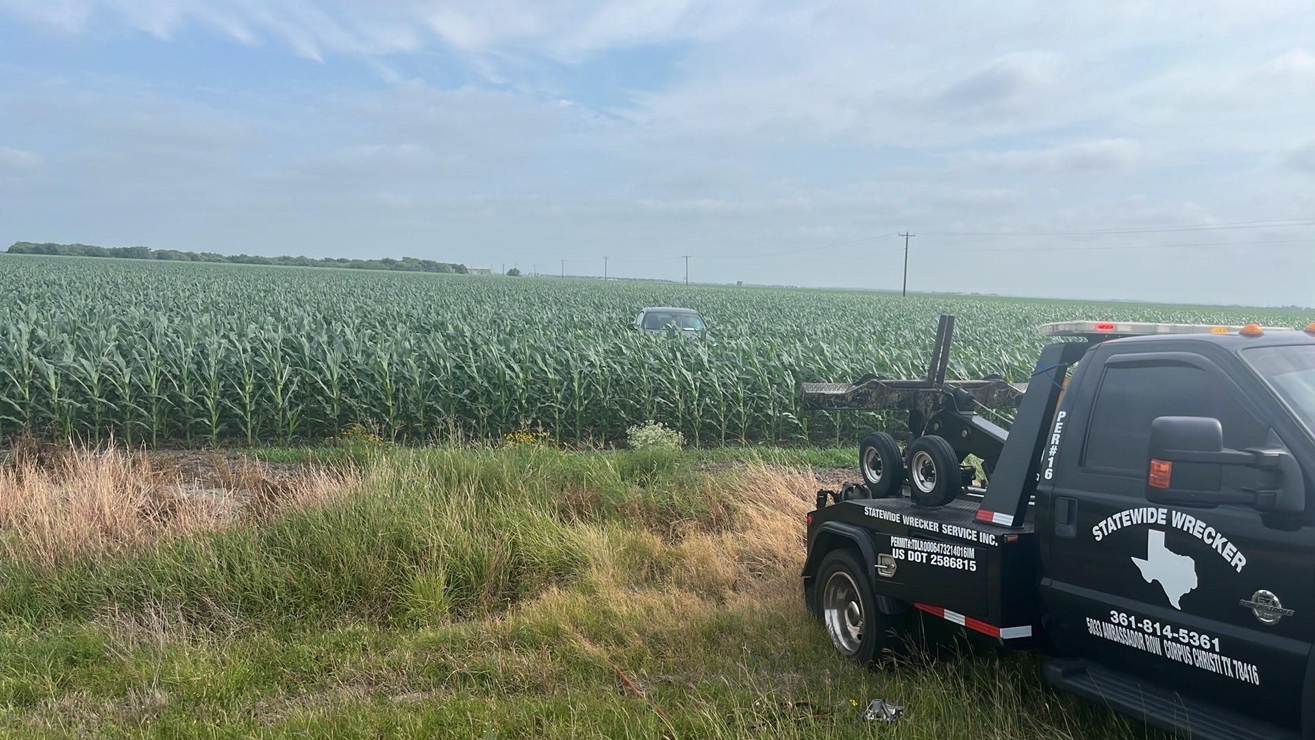 Hand attaching yellow tow strap to vehicle's undercarriage hook, outdoors.