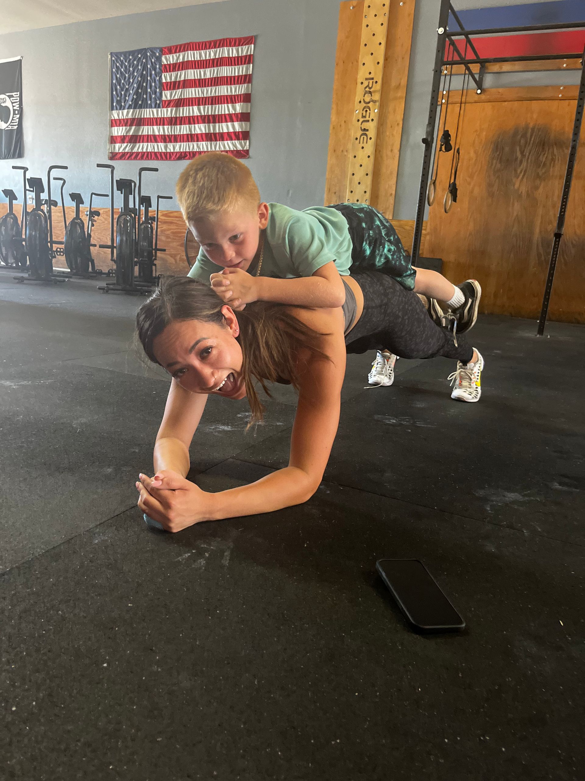 A woman and child are doing a CrossFit workout together. They are surrounded by gym equipment.