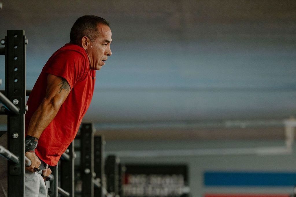 A man in a red shirt is doing push ups on a bar in a gym.