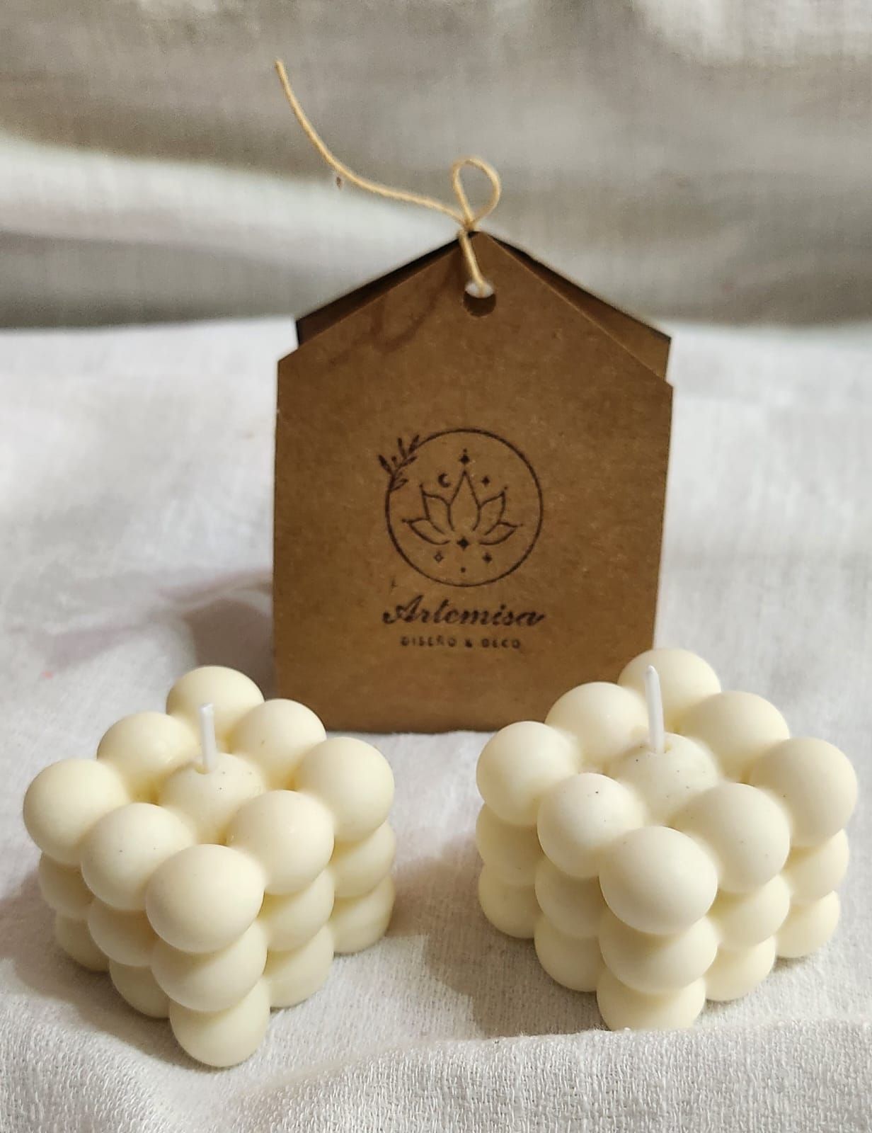 Dos velas blancas en forma de cubo de burbujas con una caja de regalo marrón.