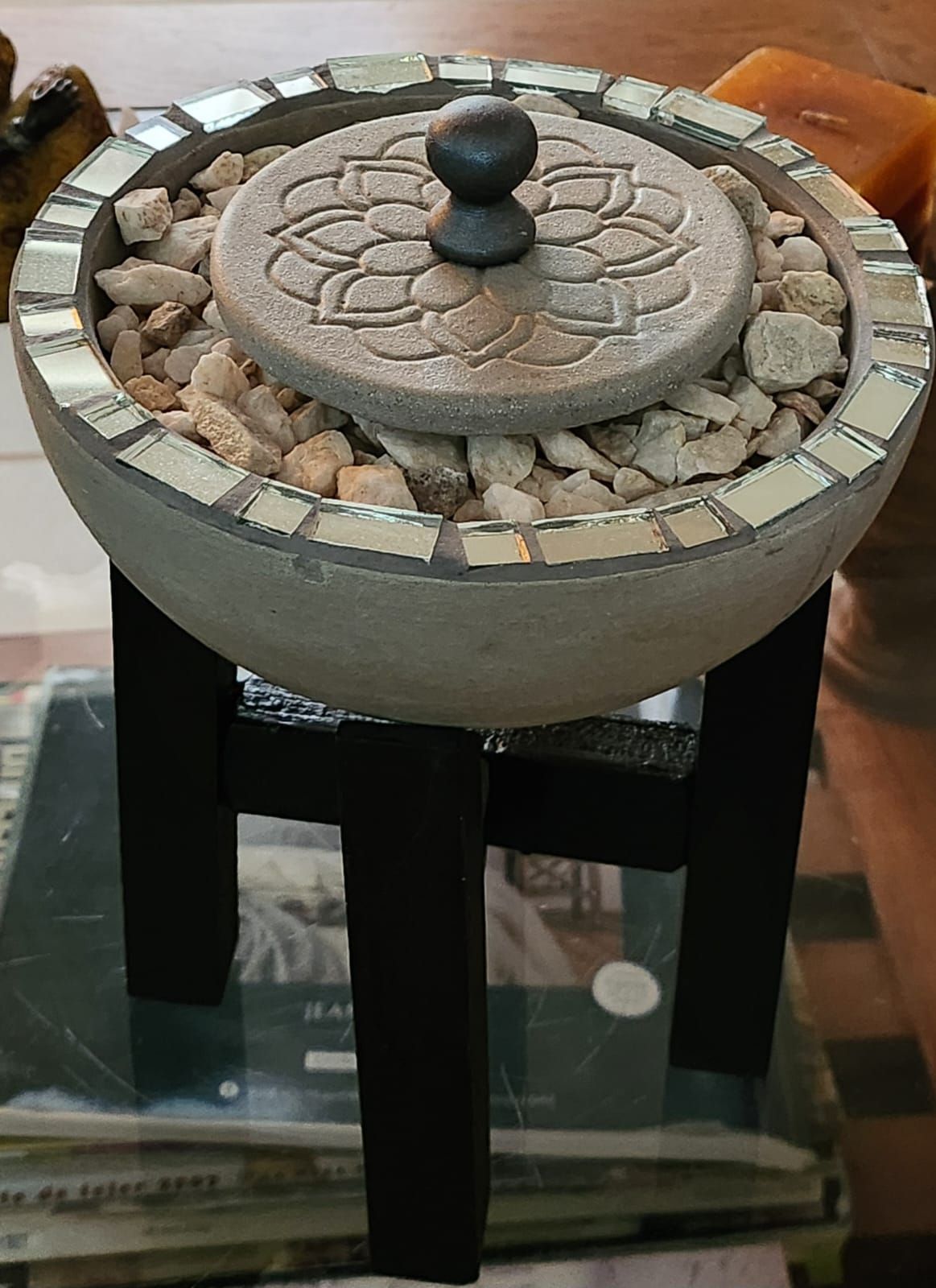 Una pequeña fuente decorativa con un cuenco de piedra, un borde de mosaico y un pequeño soporte negro.