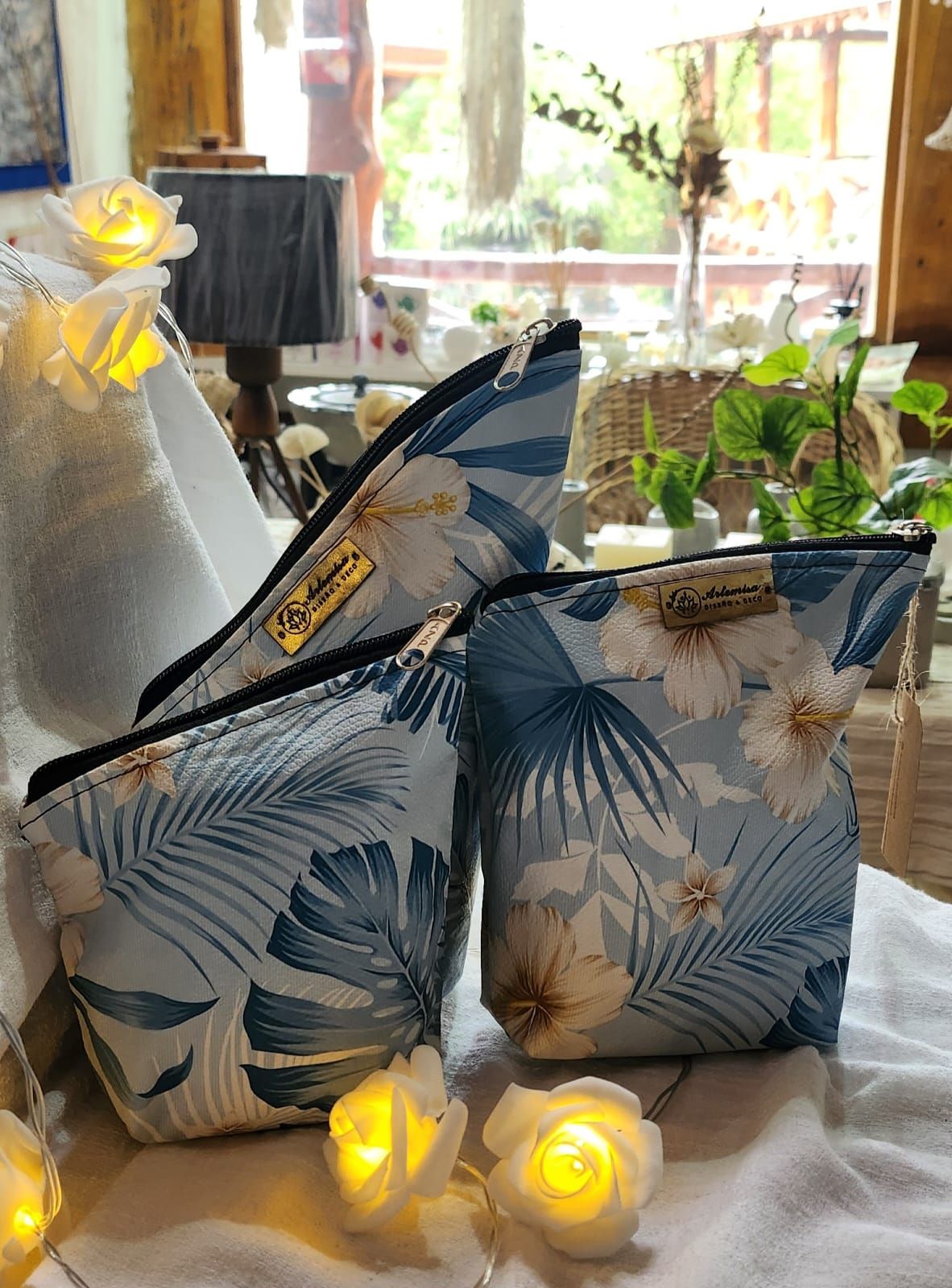 Tres neceseres azules con estampado floral y cremalleras negras, iluminados con luces de hadas en forma de rosa.