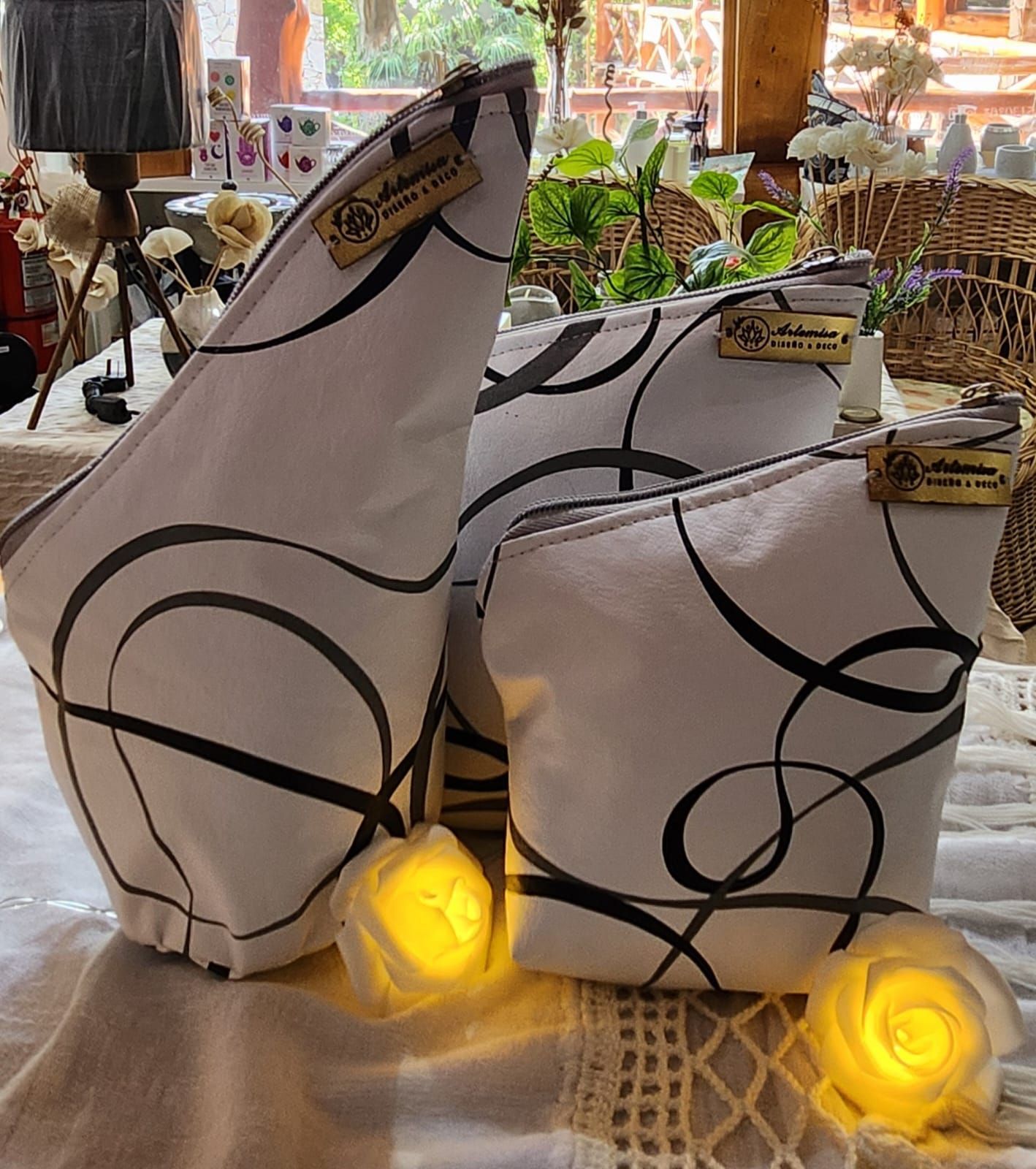 Tres neceseres blancos con un diseño de garabatos negros, delante de una ventana con luces rosas brillantes.