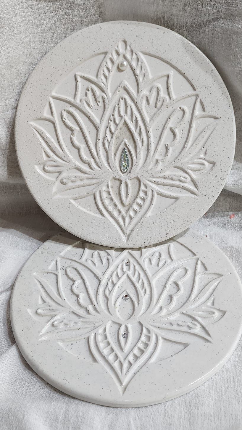 Dos posavasos blancos y redondos con diseños de flores de loto en relieve, sobre una superficie blanca.