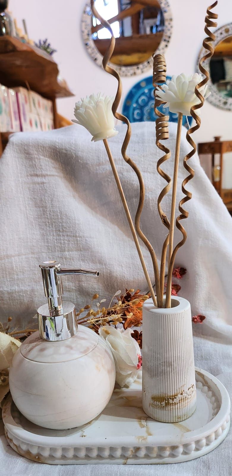 Dispensador de jabón blanco y jarrón con detalles dorados y varillas decorativas sobre una bandeja blanca.