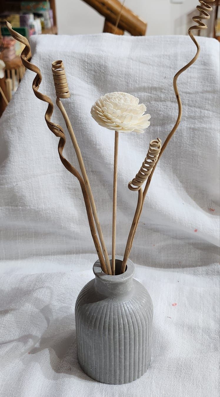 Jarrón gris con flores secas y tallos retorcidos sobre tela blanca.