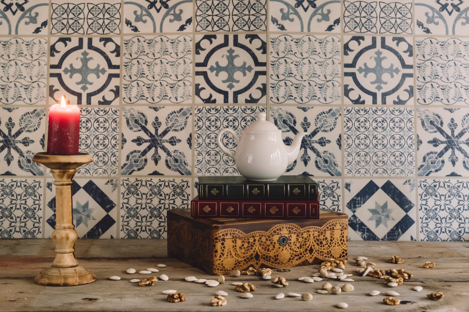 Una vela en un candelabro junto a libros, una tetera y nueces sobre una superficie de madera