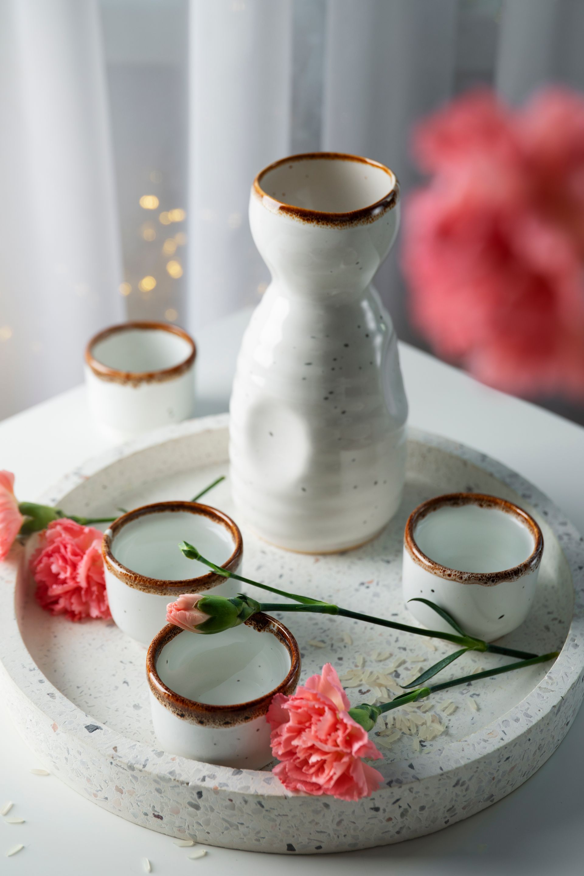Sake servido en una bandeja, con una jarra y tazas pequeñas, decorado con flores rosas.