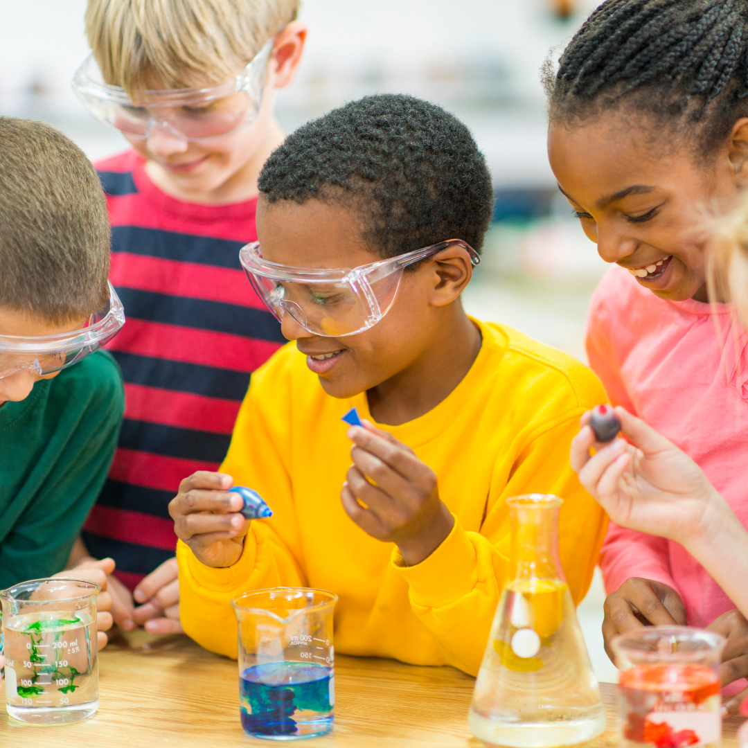 a group of children are sitting at a table with beakers and glasses .