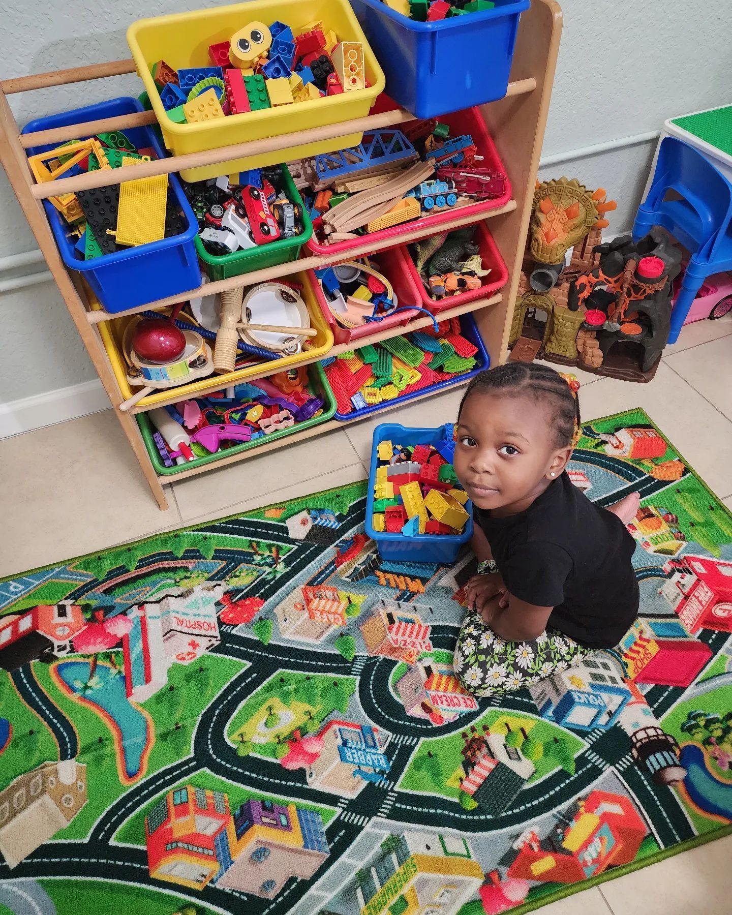 A little girl is sitting on a rug in a room filled with lots of toys.