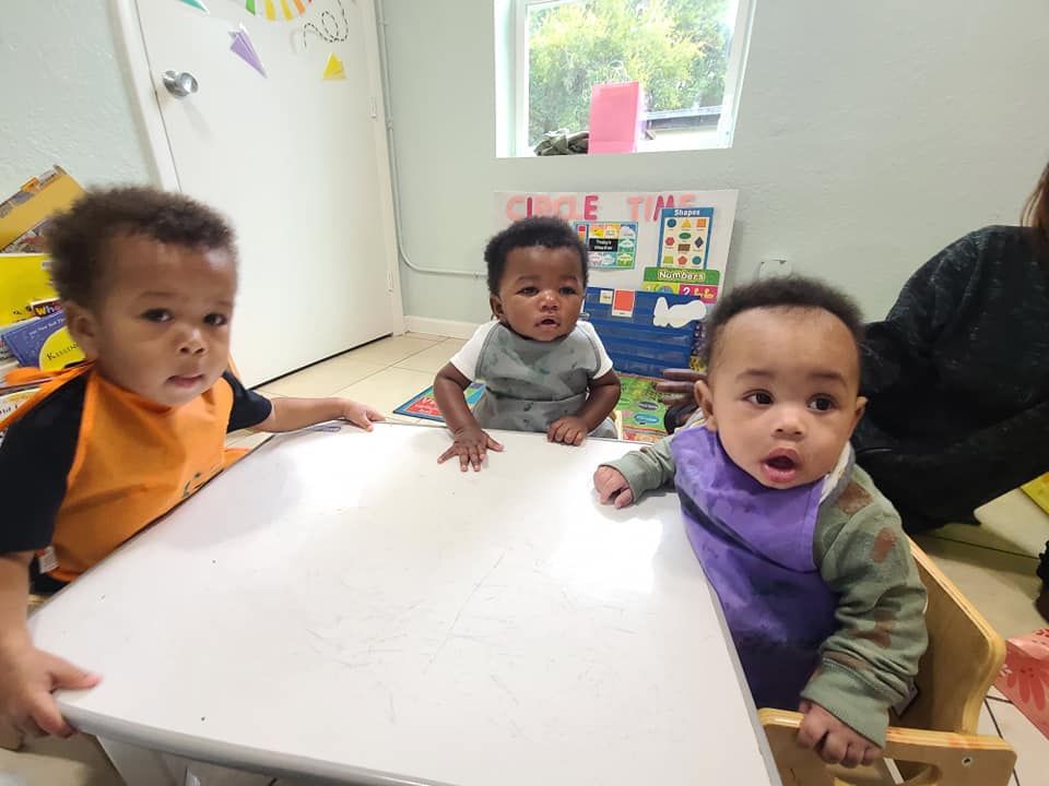 Three babies are sitting at a table in a room.