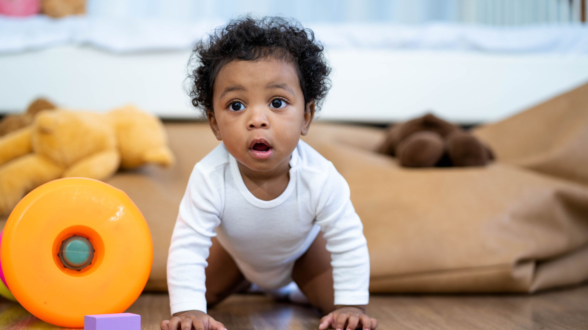 a baby is crawling on the floor next to a ball and blocks .