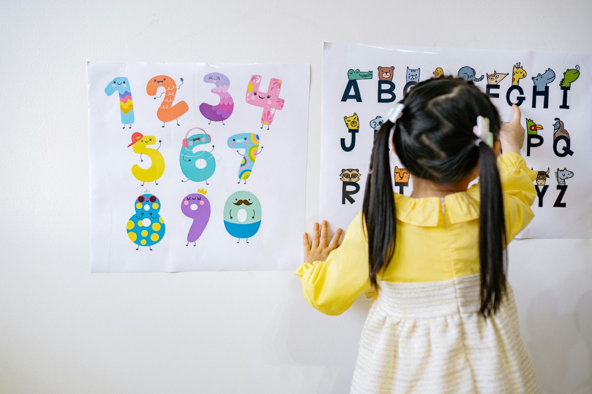 A little girl is standing in front of a wall with numbers and letters on it.