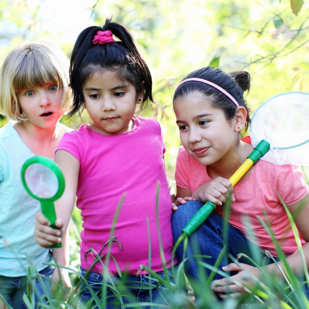 Three young girls are looking through a magnifying glass in the grass.