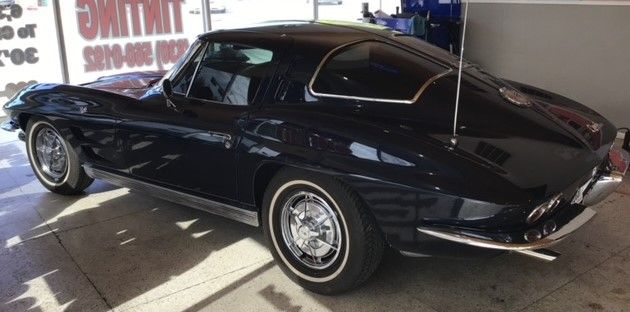 Black classic Corvette with white wall tires parked indoors.