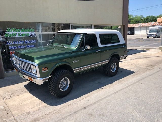 Green and white vintage Chevrolet Blazer parked outside a business on a sunny day.