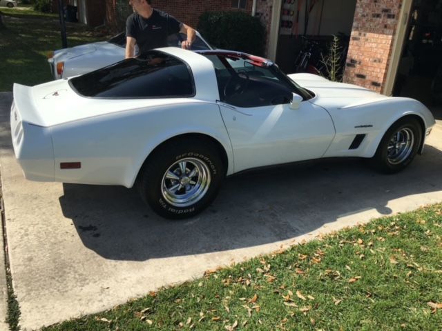 White classic Corvette parked on a driveway, person near the car.