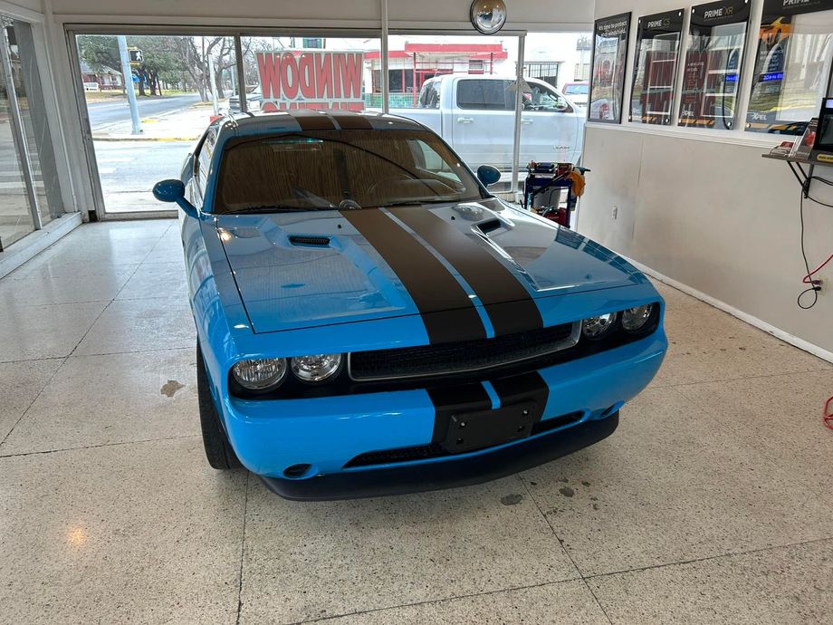 Blue Dodge Challenger with black racing stripes inside a shop.