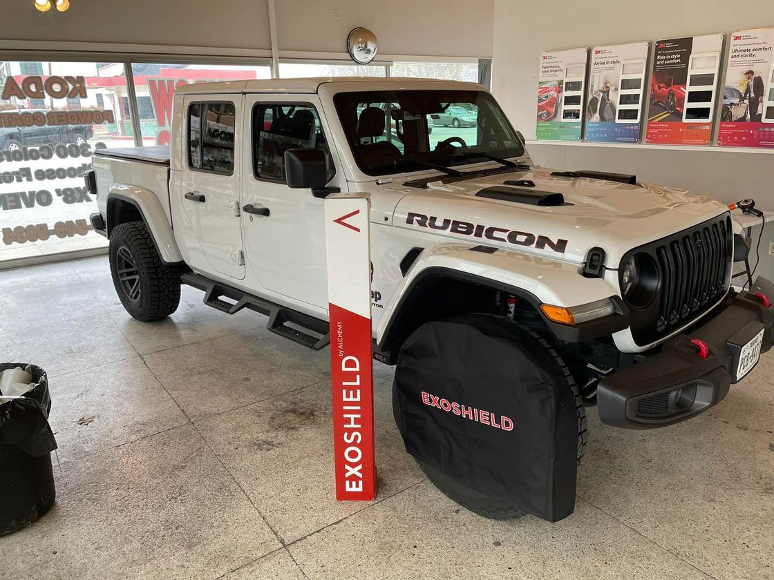 White Jeep Gladiator Rubicon displayed in a shop with an Exoshield sign and cover.