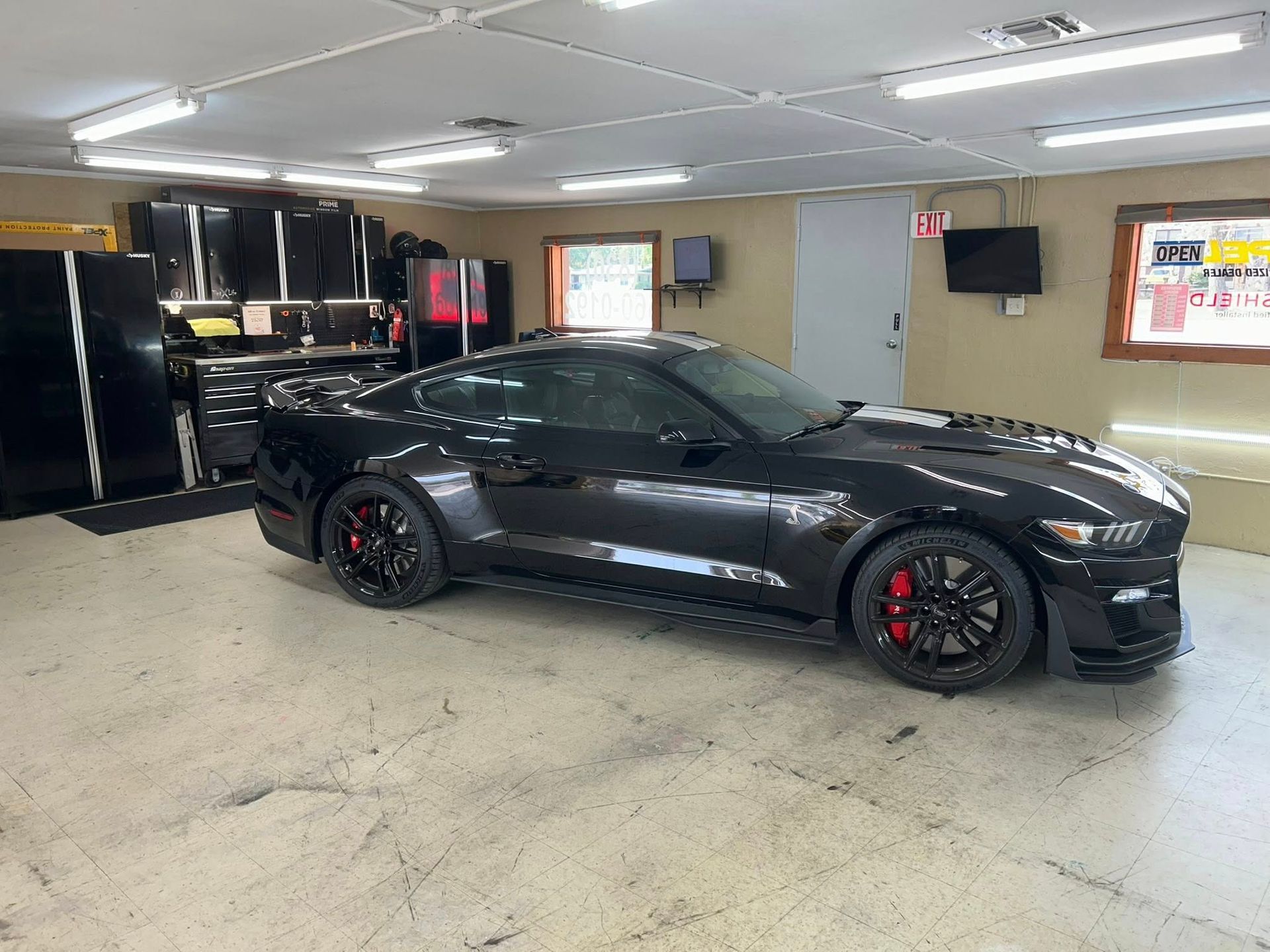 Black Mustang sports car inside a garage with black cabinets and concrete floor.