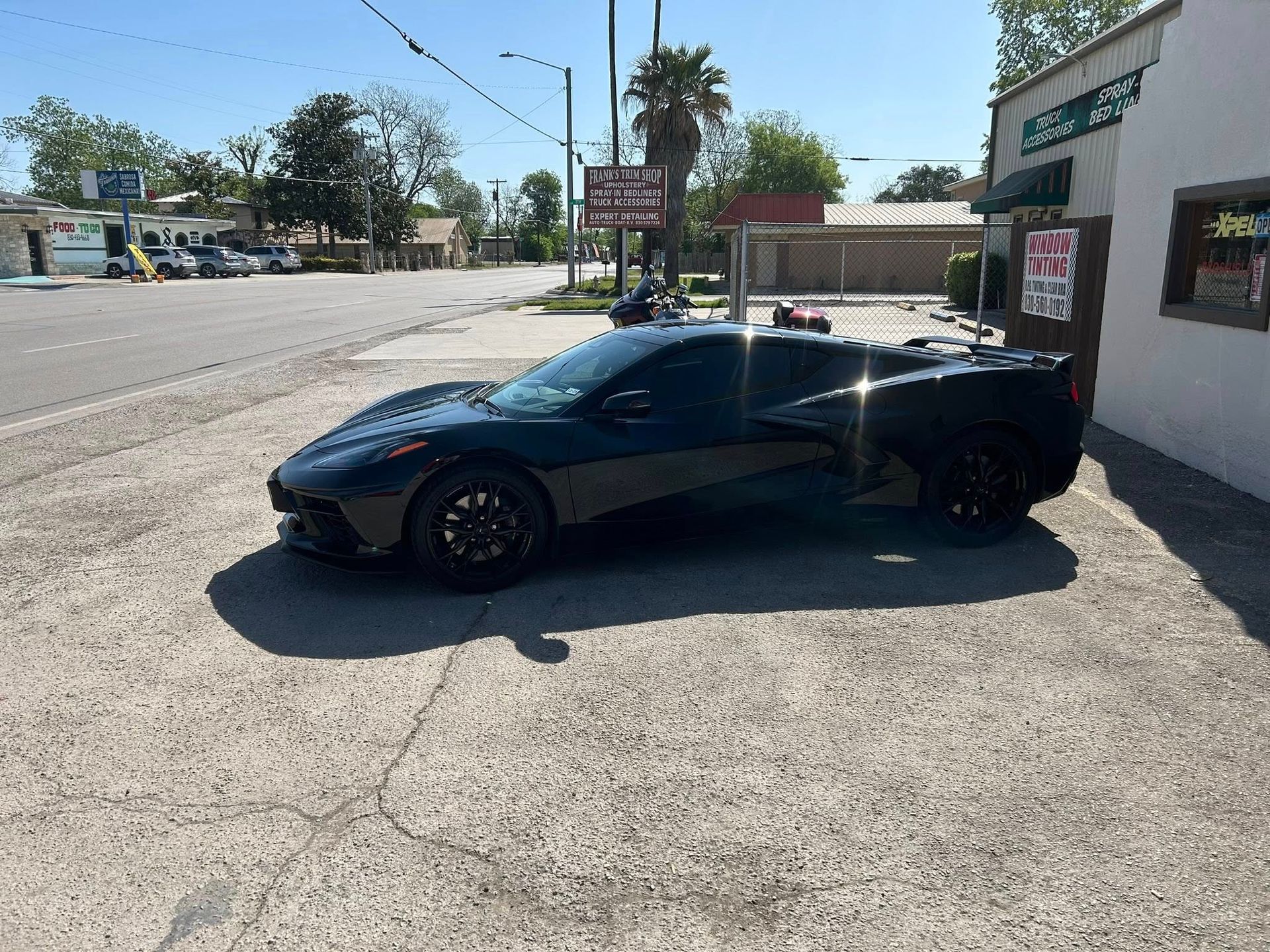 Black sports car parked near a building on a sunny street.