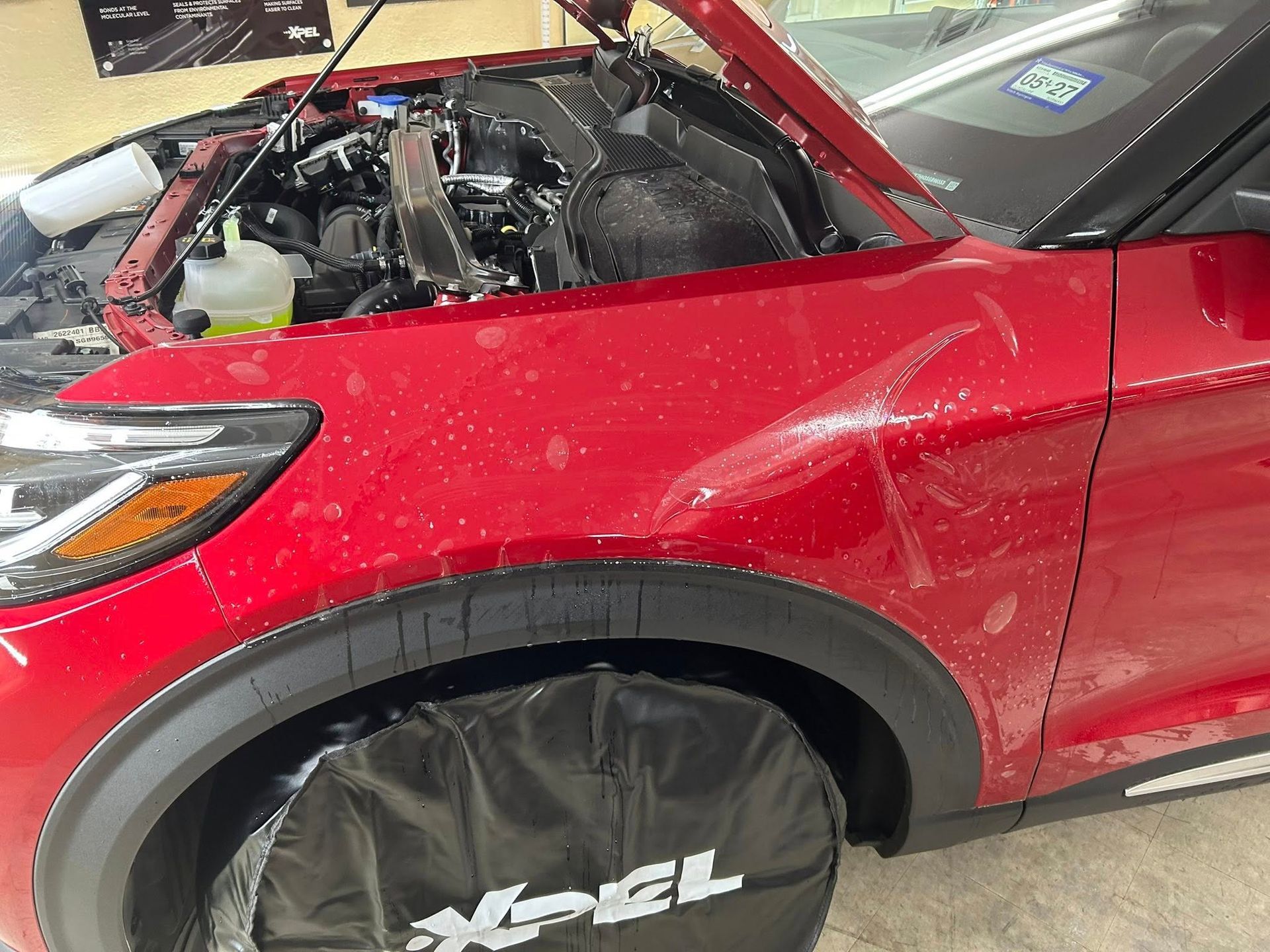 Red car with hood open, covered in water.  Front fender protected with black Xpel cover.