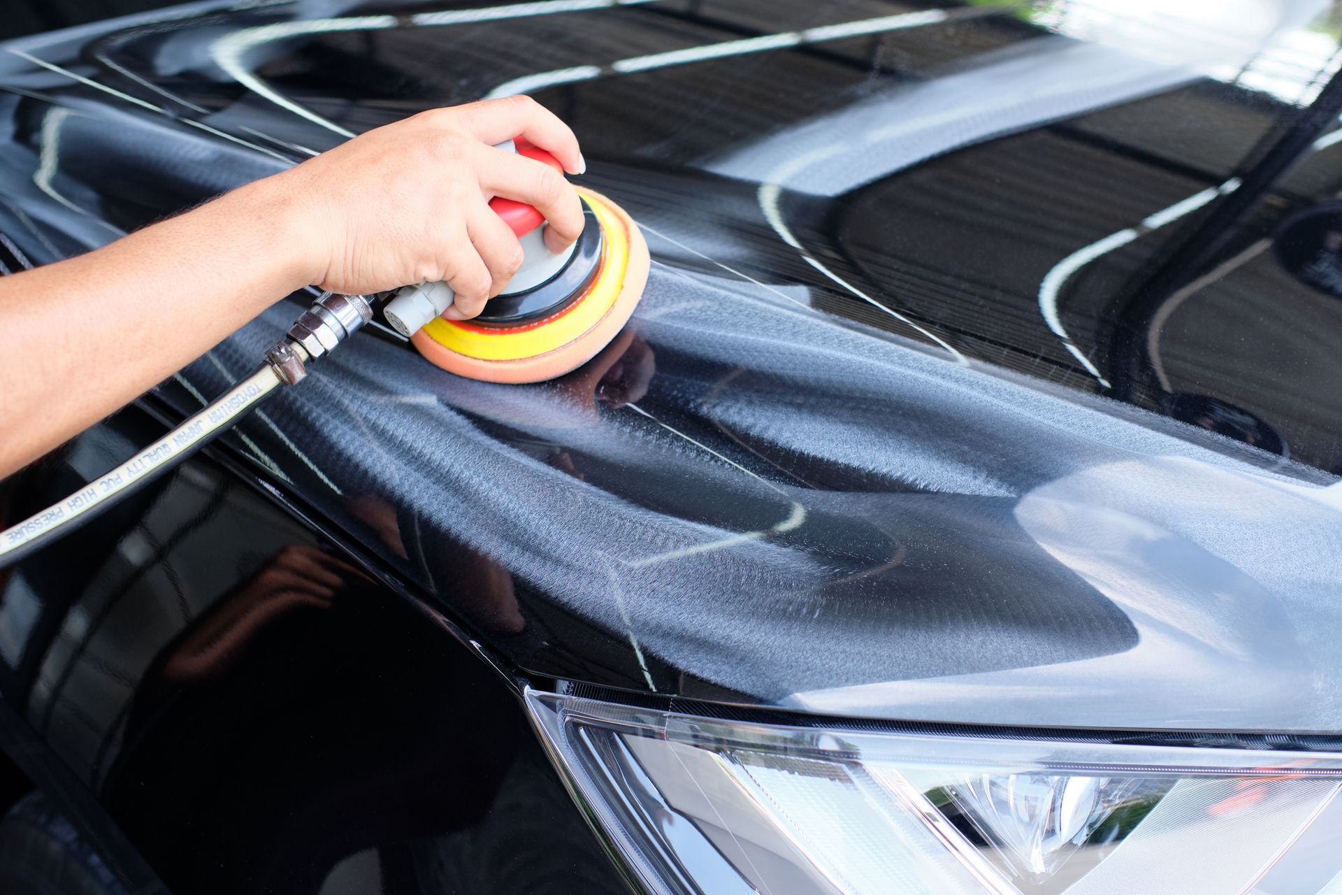 Person polishing a black car hood with a power buffer.