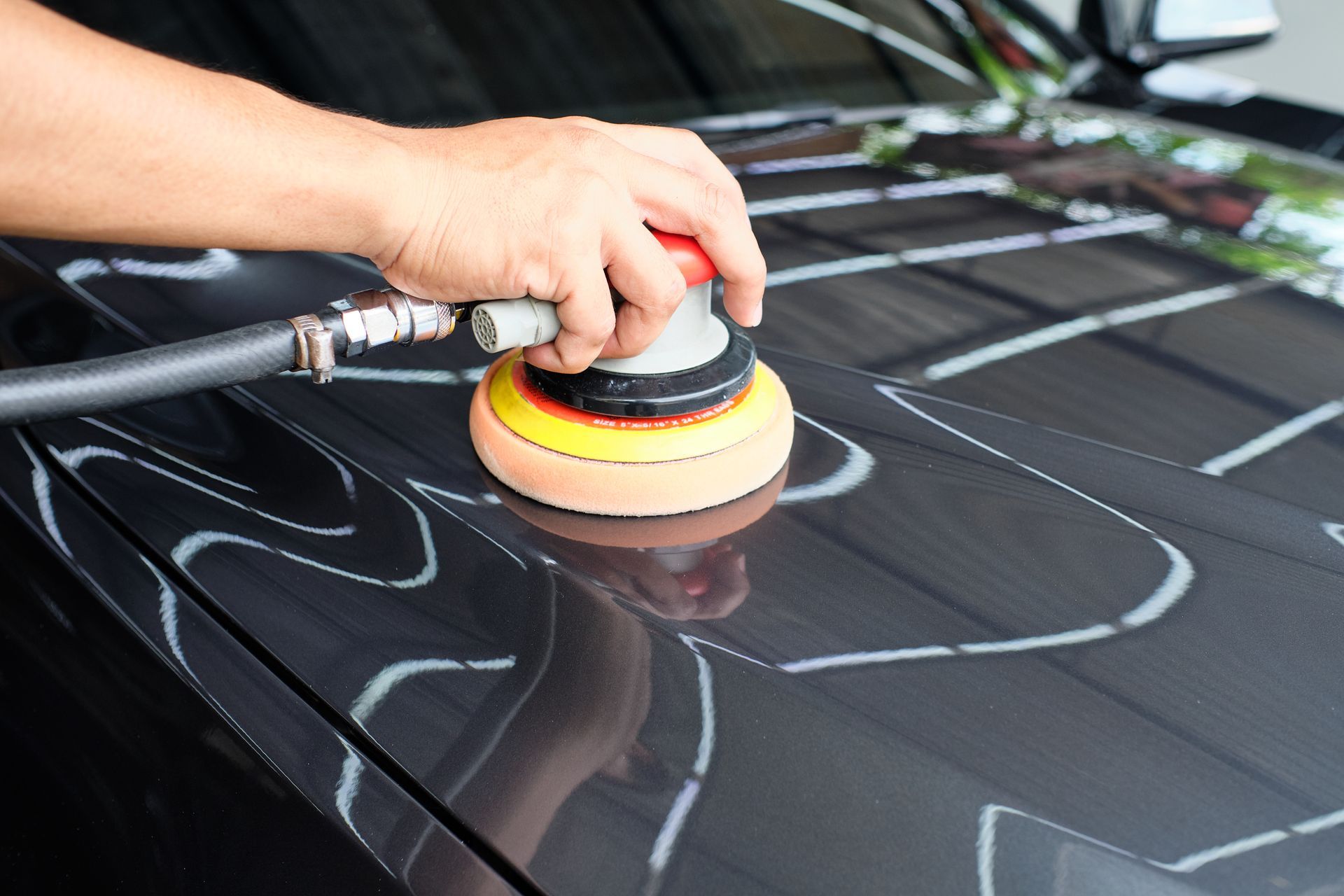 A person polishes a black car with an electric polisher.