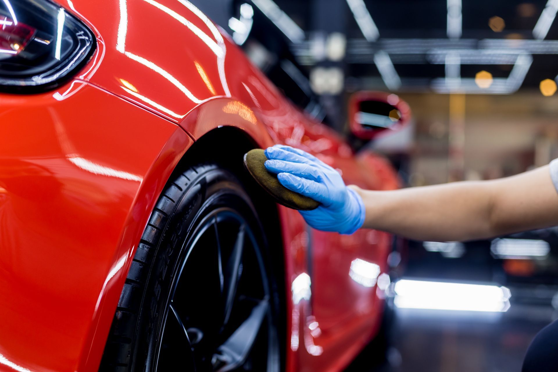Person in blue glove waxing a shiny red car tire in a garage.