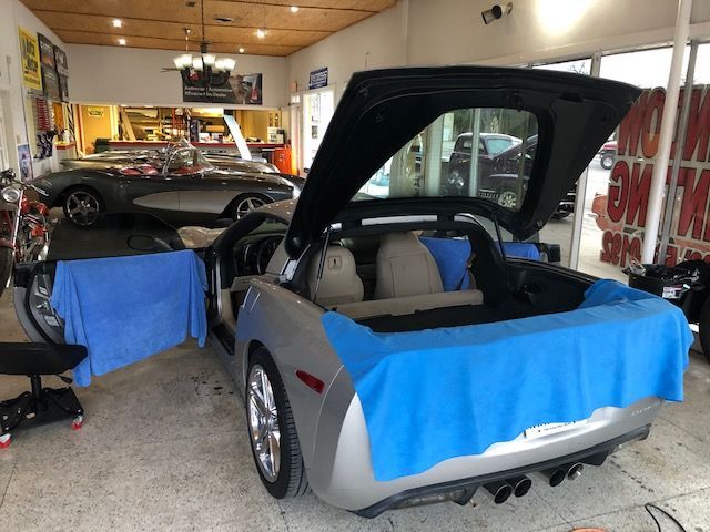 A silver Corvette with its doors and trunk open, protected with blue towels, inside a shop.