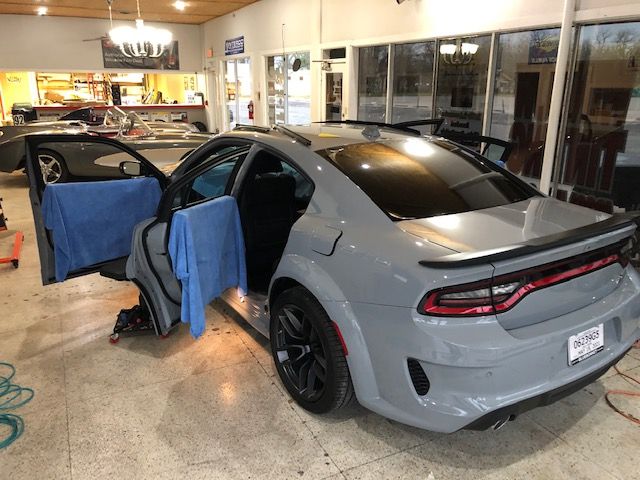 Gray Dodge Charger with open doors, in a shop setting, protected with blue cloths, black wheels.