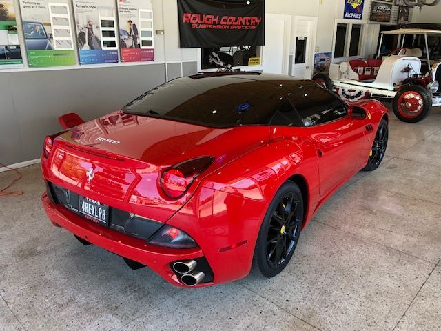 Red Ferrari sports car in a garage, with black wheels and tinted windows.