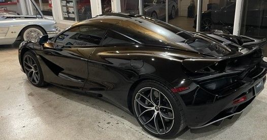 Black McLaren sports car parked in a garage, angled view of the rear.