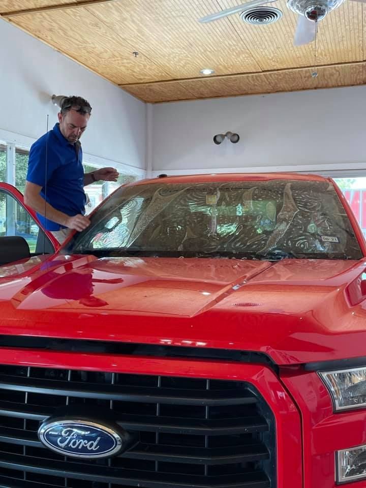 Man applying film to the windshield of a red Ford truck indoors.