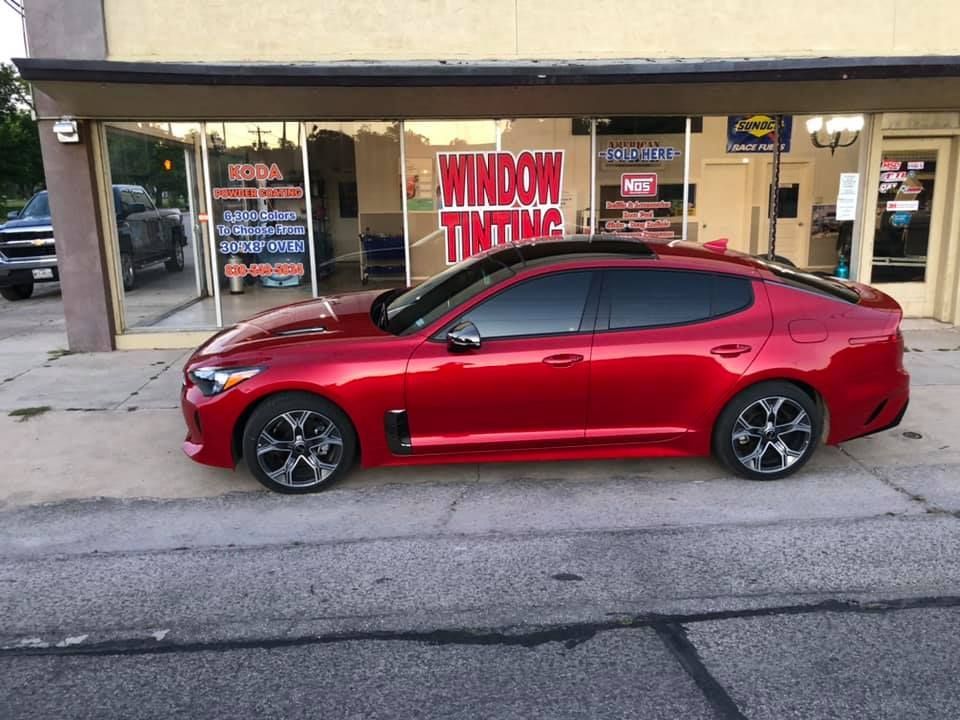 Red Kia Stinger parked outside a window tinting business.