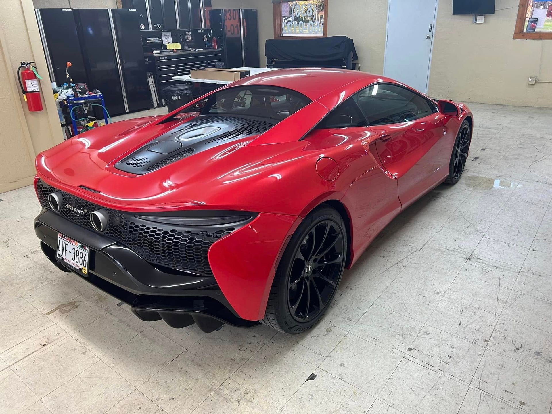 Red McLaren sports car in a garage, black wheels, black accents.