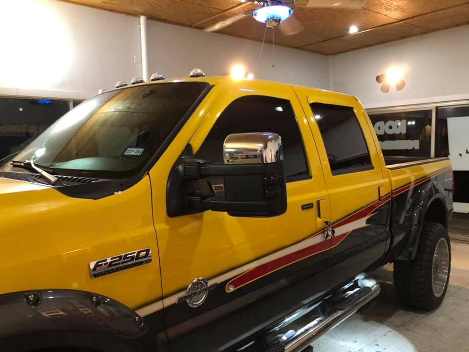 Man applying film to the windshield of a bright red Ford truck inside a shop.