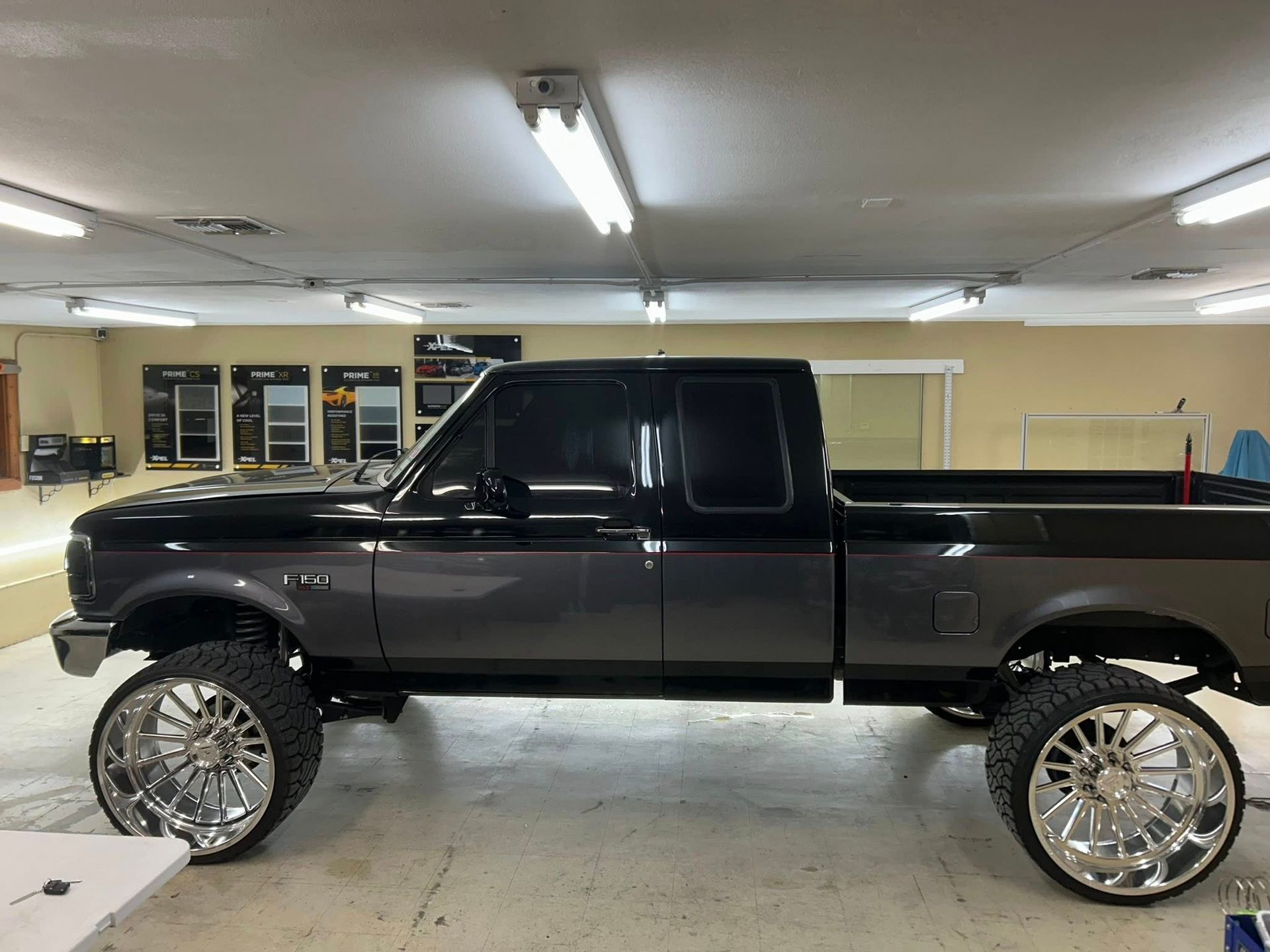 Two-tone gray lifted pickup truck with chrome wheels in a garage.